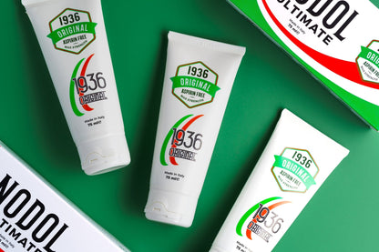 Three 75ml tubes of Nodol Aspirin-Free Pain Cream, renowned for its natural formula, are set against a green background, showcasing labels that read "Aspirin Free" and "Made in Italy." Two tubes lie flat while one stands upright with partial packaging visible nearby, providing effective relief for muscle pain.